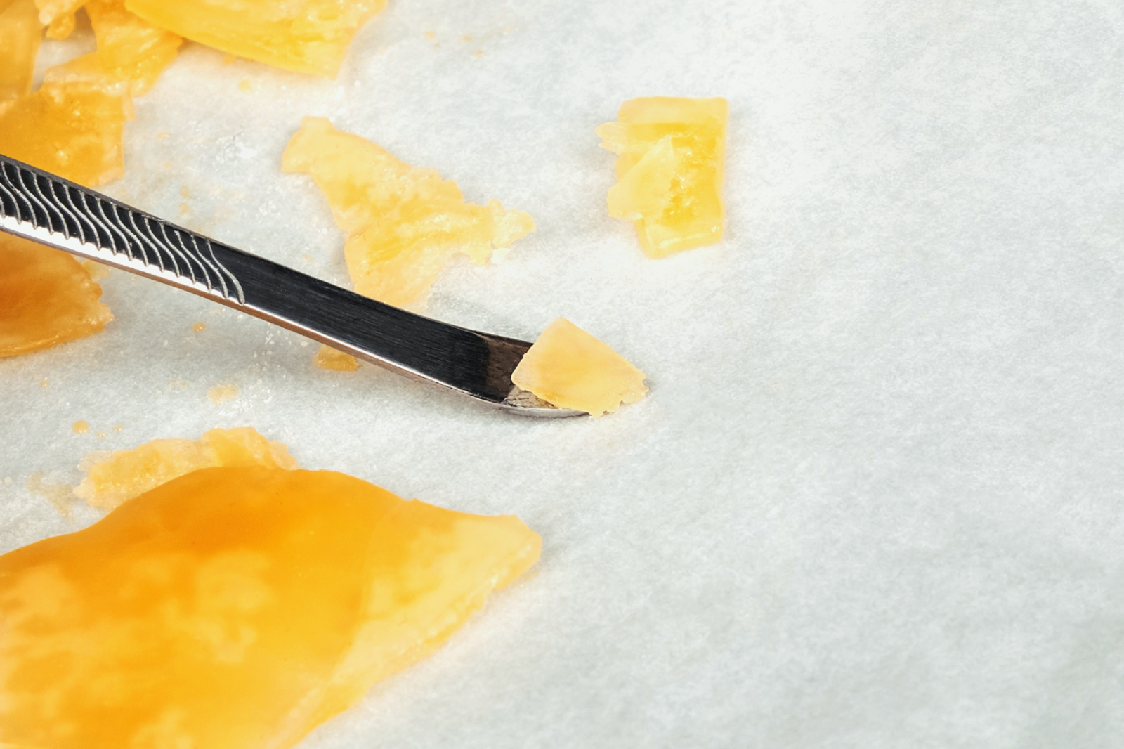 Photo of a solid amber/yellow cannabis extract alongside a metal dabbing tool.