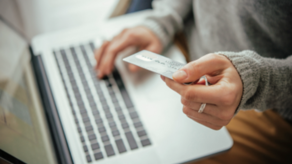 Photo illustrant une main tenant une carte de crédit et un ordinateur pour effectuer une transaction en ligne.